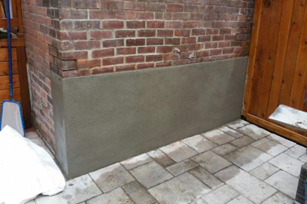 Fresh parging on the lower section of a brick wall beside a paved area